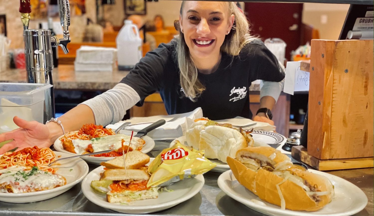 A Luigi's server presenting plates of subs, pasta and garlic bread
